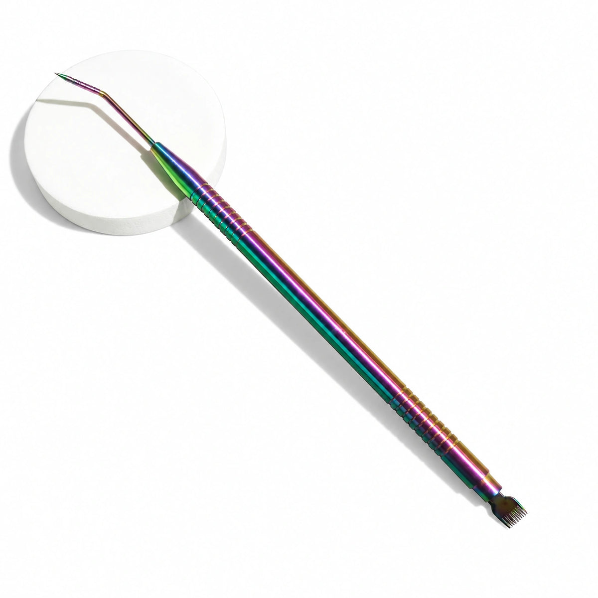 Lomansa rainbow dual-ended lash lift tool with an angled tip and comb end, displayed on a white round pedestal.