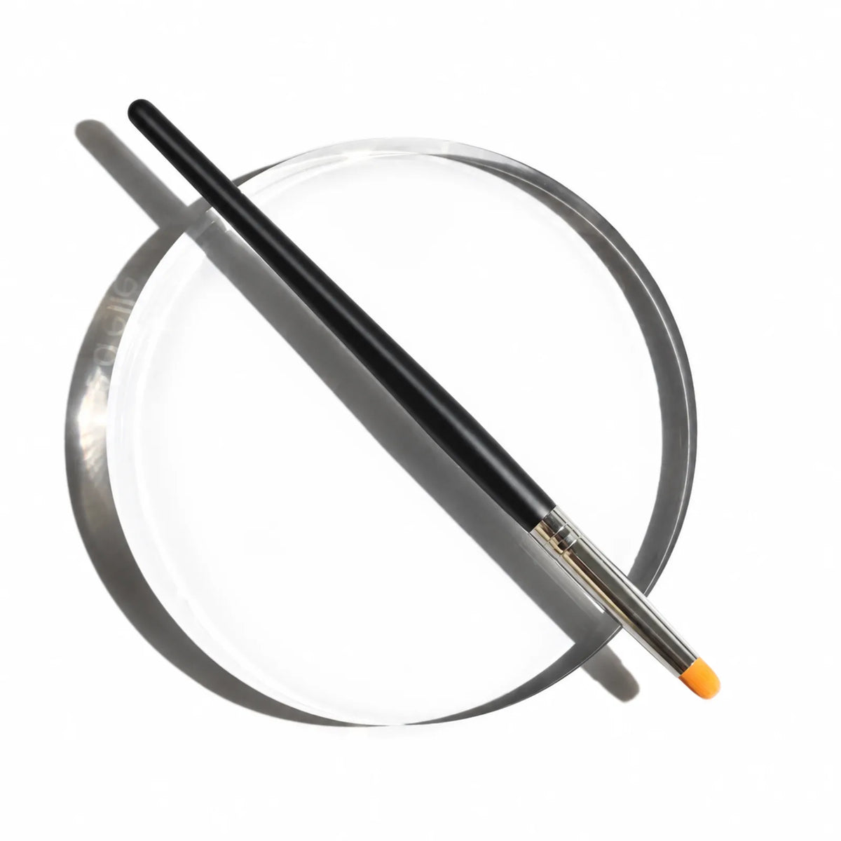 Black-handled Lomansa lash lift applicator brush with a silver ferrule and orange tip resting on a clear round tray.