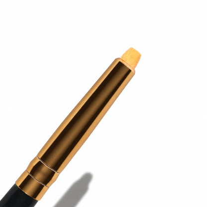 Close-up of a Lomansa lash lift applicator brush with a gold ferrule, black handle and short angled orange bristles.