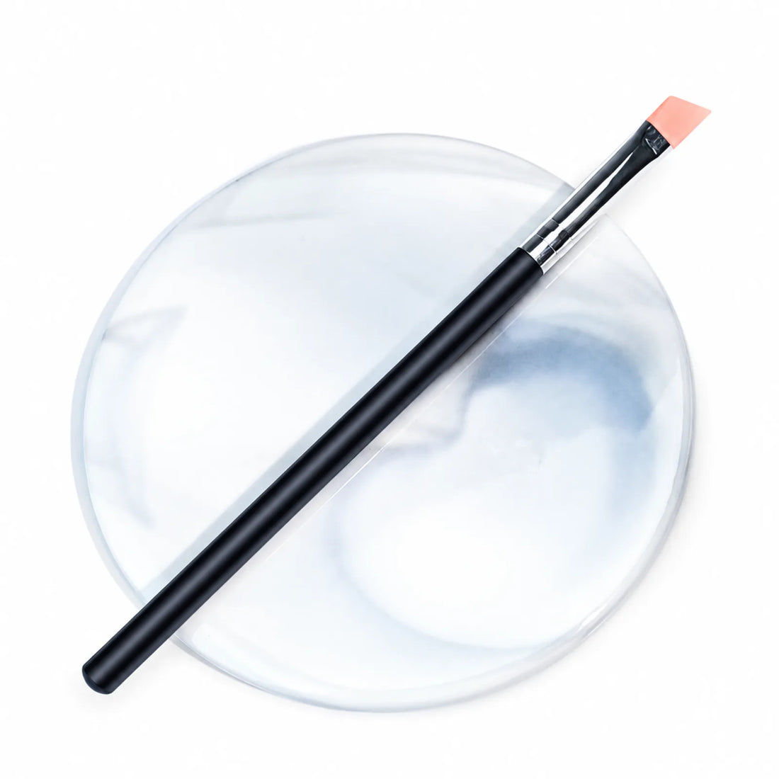 Lomansa black-handled angled silicone applicator brush with peach tip displayed on a round marble-patterned tray.

