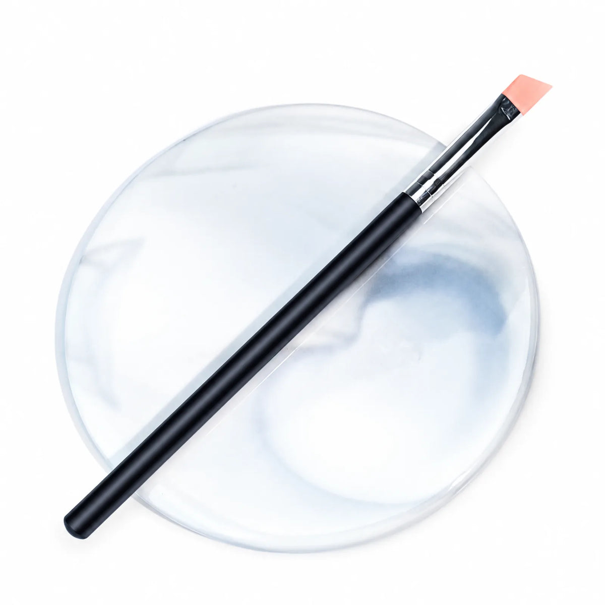 Lomansa black-handled angled silicone applicator brush with peach tip displayed on a round marble-patterned tray.
