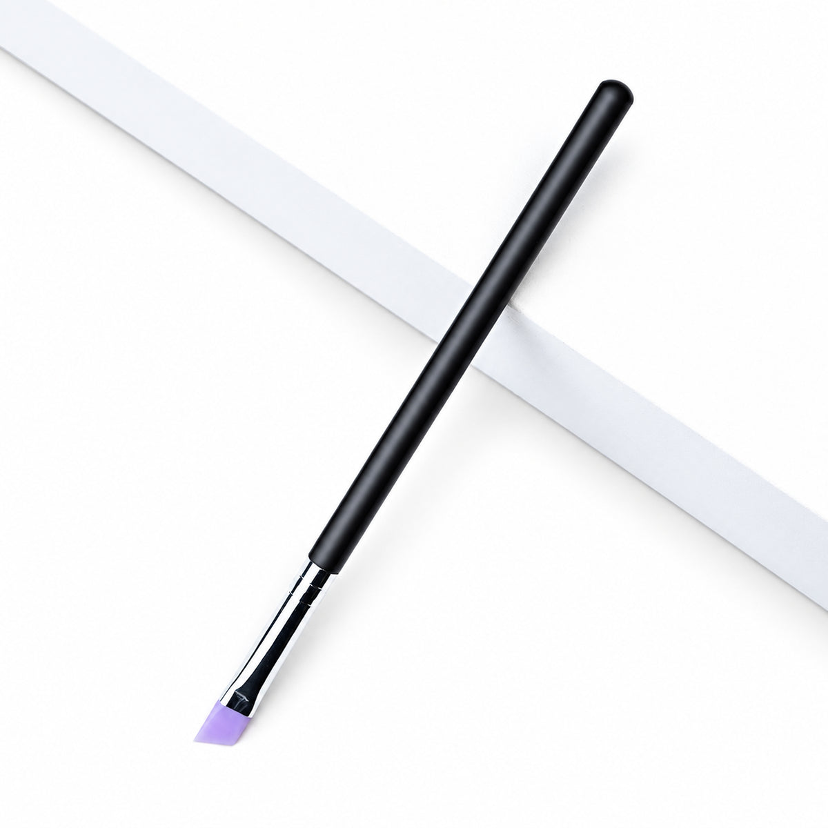 Lomansa angled silicone applicator brush with a purple tip, silver ferrule and black handle on a white geometric surface.