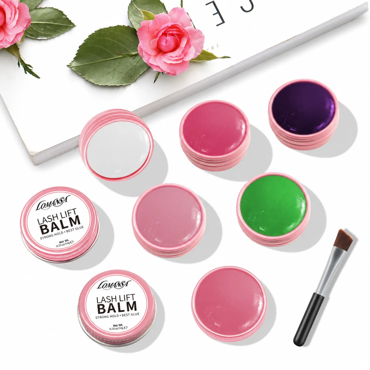 Assorted LOMANSA lash lift balm pots with two labeled tins, an angled brush and pink roses on a white background.