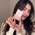 Woman holding a peach and white Lomansa lash and brow tint kit box beside her face.