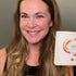Smiling woman holding a white Lomansa lash lift kit box with orange accents.