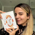 Blonde woman holding a white Lomansa lash perm kit box with orange graphics.